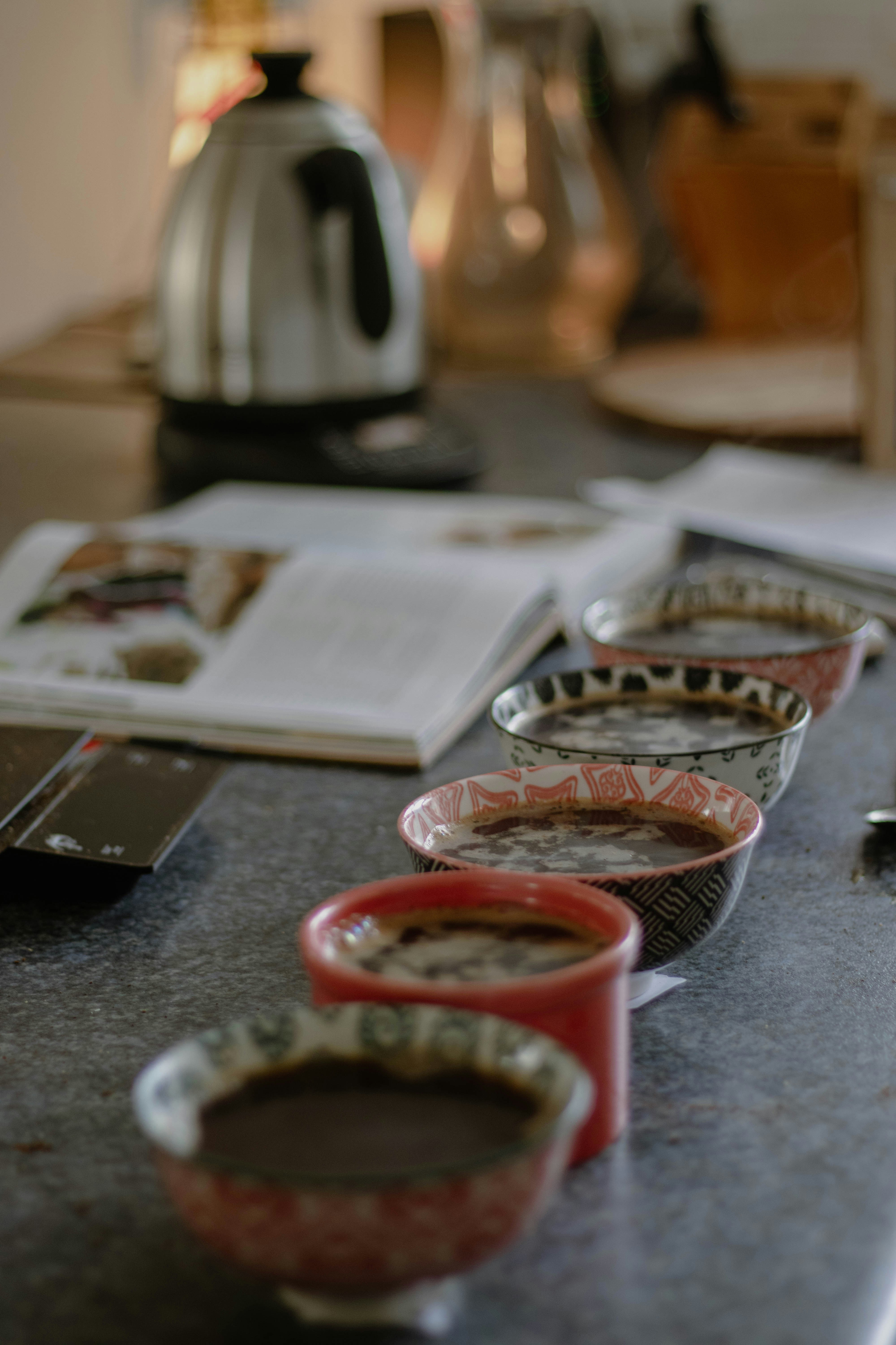 coffee cupping, cups lined up diagonally with brewing materials in the background like kettle and scale